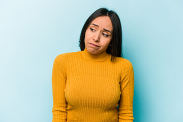 Young hispanic woman isolated on blue background shrugs shoulders and open eyes confused.
