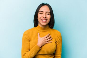Young hispanic woman isolated on blue background laughs out loudly keeping hand on chest.