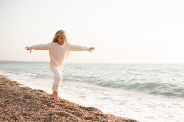 Fototapeta na wymiar Happy smiling kid girl 5-6 year old wear knit sweater and pants running over sea shore outdoors. Cheerful little toddler having fun at beach. Summer season. Childhood. Happiness.