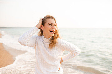 Fototapeta na wymiar Laughing happy blonde woman wear white knit sweater resting over sea shore baat background. Summer season. Happiness. Cheerful adult girl.