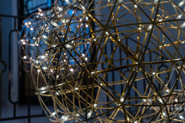 Golden metallic chandelier in form of large ball with lamps in restaurant interior. Large art glowing sphere.