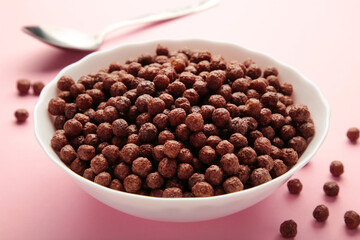 Chocolate cereal corn balls in a white bowl on a pink background.