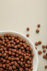 Chocolate cereal corn balls in a white bowl on a grey background. Vertical photo.