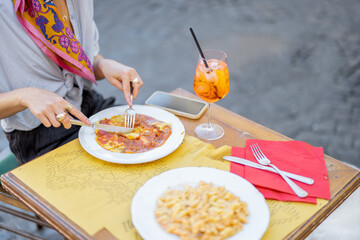 Woman eating ravioli with bolognese sause and drinking Spritz Aperol at restaurant outdoors, close-up view. Concept of italian gastronomy