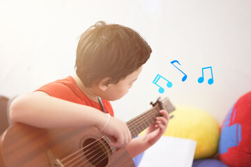 The boy plays the guitar with his left hand, a song by himself, on the sofa, in the bedroom, reading the sheet music.