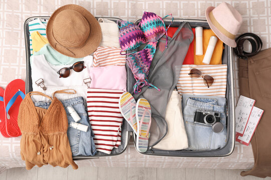 Open suitcase with summer clothes, accessories and shoes on bed, flat lay