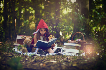 Books can transport us to the most magical places. Shot of a little girl in a red cape reading a...