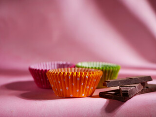 Bun cases in different colors with chocolate for baking on pink background