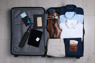 Folded clothes, shoes and accessories in open suitcase on wooden background, top view. Packing for...