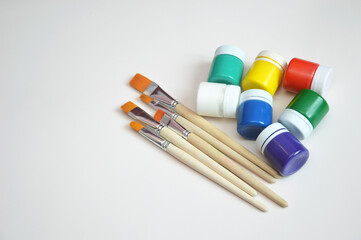 Multi-colored jars of gouache paint and synthetic brushes. A set of objects for drawing. Hobby,...