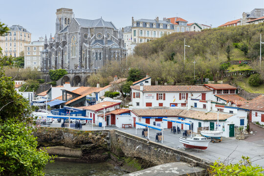Photo du vieux port de Biarritz avec bateaux et les crampottes (cabanes typiques). Vue de l'Eglise sainte eugénie de Biarritz en arrière plan