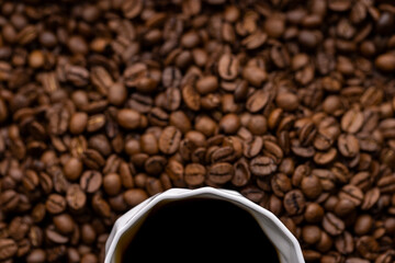 A partially visible white cup of black coffee surrounded by coffee beans