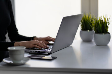 Businesswoman working on the laptop during sunny day in the office. Cup of coffee, artificial grass, mobile phone and pen included. Free space for business logo.  Home office initiative. 