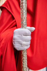 Detail of the white gloved hand of a Nazarene or penitent, holding a silver wand of command....