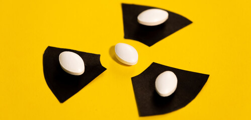 Four anti-radiation pills based on iodine on a yellow background and the radiation warning sign