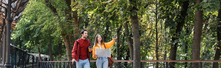 Traveler holding takeaway drink and binoculars near girlfriend with map on urban street, banner.