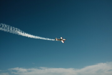 A small plane maneuvers in a blue sky with a contrail. High quality photo