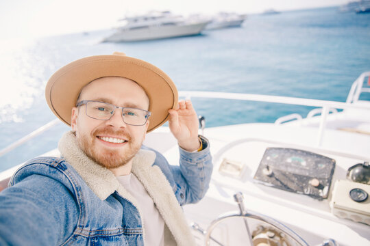 Happy caucasian man in hat taking selfie photo on white luxury boat yacht at vacation