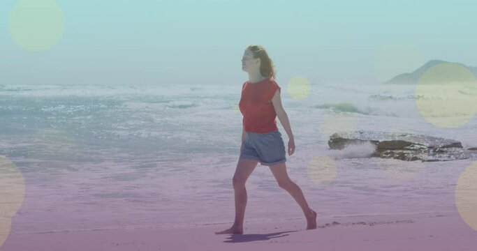 Animation of light spots over caucasian woman walking on beach