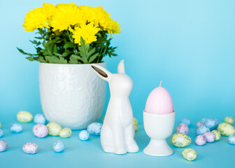 Easter card. Easter porcelain bunny, painted eggs and a yellow flower in a white pot on a blue background. Yellow-blue concept.