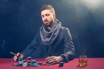 A wealthy mature man drinking brandy and playing poker with the excitement in a casino. 