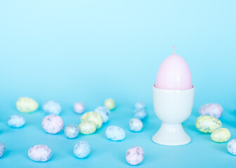 Easter card. Pink egg candle in a porcelain egg stand, colorful eggs on a blue background. Pastel colors