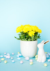 Easter card. Easter porcelain bunny, painted eggs and a yellow flower in a white pot on a blue background. Yellow-blue concept.