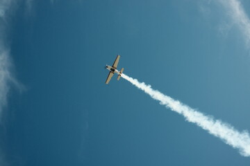  A small plane maneuvers in a blue sky with a contrail. High quality photo