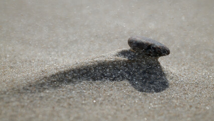 Fototapeta na wymiar Kamień po silnej wichurze leży na utworzonej górce z morskiego piasku. Całość zasnuta ziarnami piasku unoszonymi przez wichurę. Makro, burza piaskowa, close-up, rozmyte tło, bokeh