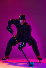 Full-length portrait of professional male hockey player training, prctising isolated over pink background in neon light