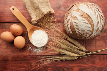 Round rye bread, rye in burlap, ears of corn, rolling pin, brown eggs, wooden spoon with flour. Concept agricultural, farm natural food from grain. Harvest.