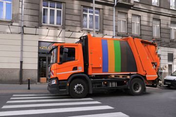 Modern orange garbage truck on city road outdoors