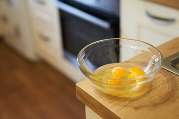 Three raw eggs in a transparent glass bowl on the background of the kitchen table. Healthy food. The concept of cooking eggs. High quality photo