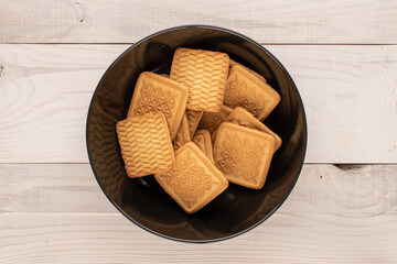 Several sugar cookies in a black plate on a wooden table, macro, top view.