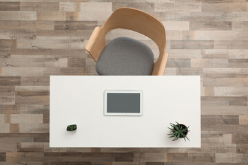 Plants and computer tablet on wooden table near armchair indoors, top view