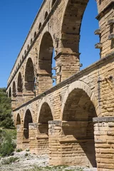 Papier Peint photo Pont du Gard Lateral view of the famous Pont du Gard- iconic ancient Roman bridge, aqueduct and engineering masterpiece in Provence, France. It is formed by three floors of arcades, massive arches and pillars.