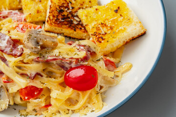 homemade fettuccine pasta with white cream sauce and garlic bread. fettuccine Carbonara made with eggs, hard cheese, cured pork, and black pepper. Italian food.