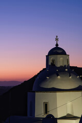 View of a beautiful whitewashed Orthodox Church and Oia Santorini in the background, while the sun...