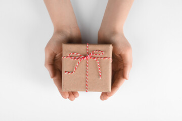 Fototapeta na wymiar Woman holding parcel wrapped in kraft paper on white background, top view