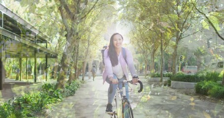 Animation of leaves over smiling asian woman cycling