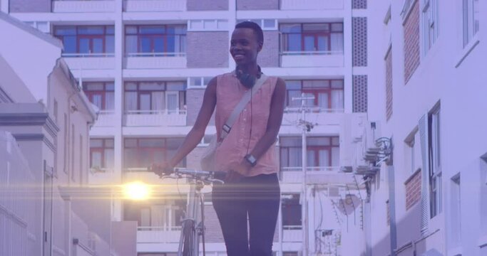 Animation of light spots over happy african american woman walking with bicycle