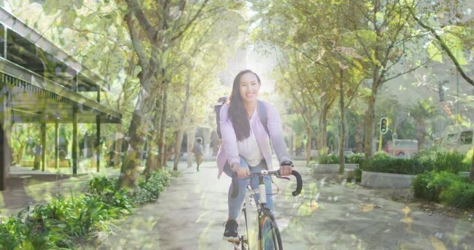 Animation of leaves over smiling asian woman cycling - Powered by Adobe