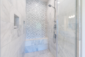Walk-in shower with white and gray pattern tile, overhead rain shower, bench seating and chrome finishes.
