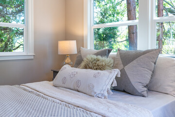 Bed fashioned with pillows in gray and white theme with window light and forest view.