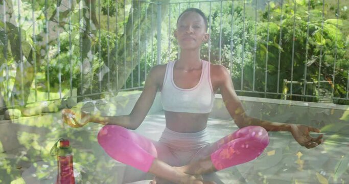 Animation of leaves over african american woman practicing yoga and meditating