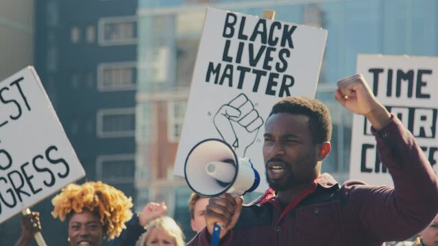 Group of protestors with megaphone holding placards and chanting slogans on demonstration march to promote black lives matter anti racist beliefs - shot in slow motion