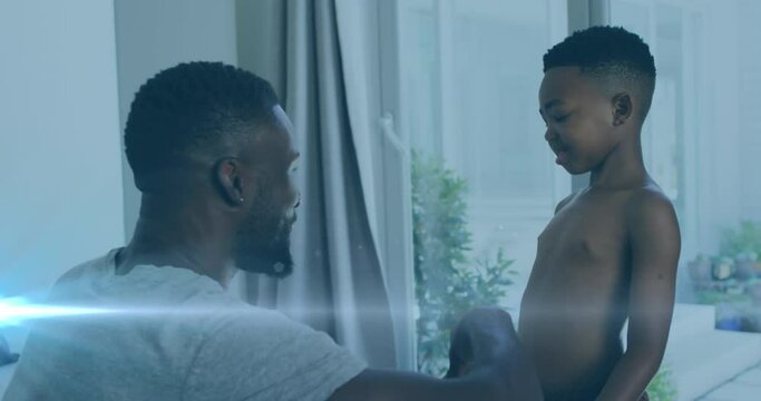 Animation of lights over happy african american father and son undressing and clapping hands