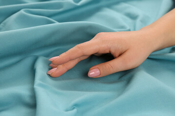 Woman touching soft turquoise fabric, closeup view