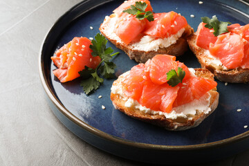Tasty bruschettas with salmon, cream cheese and parsley on grey table, closeup