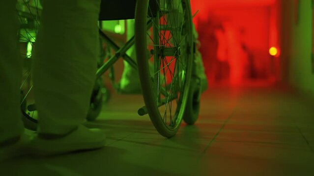A paramedic is driving a mad male patient in wheelchair down corridor in mental hospital. Ill person in straitjacket is going crazy. Concept of paranoia or schizophrenia and madness. Wheels close up.